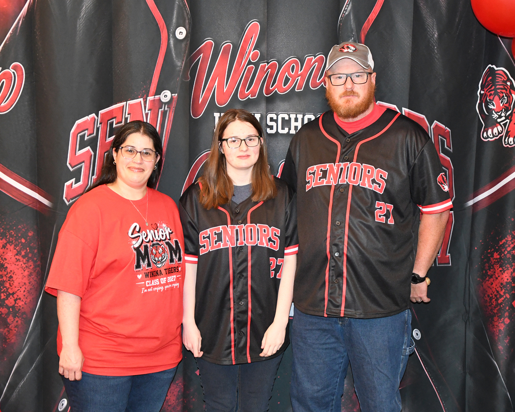 Three individuals pose for a picture in front of a backdrop with "Winona School Seniors" and red flames.