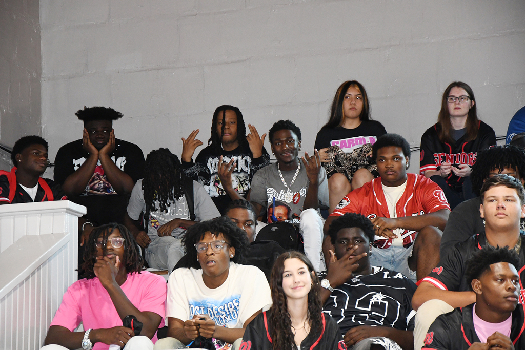 A group of young people in various colors and styles of clothing sit in a stadium.