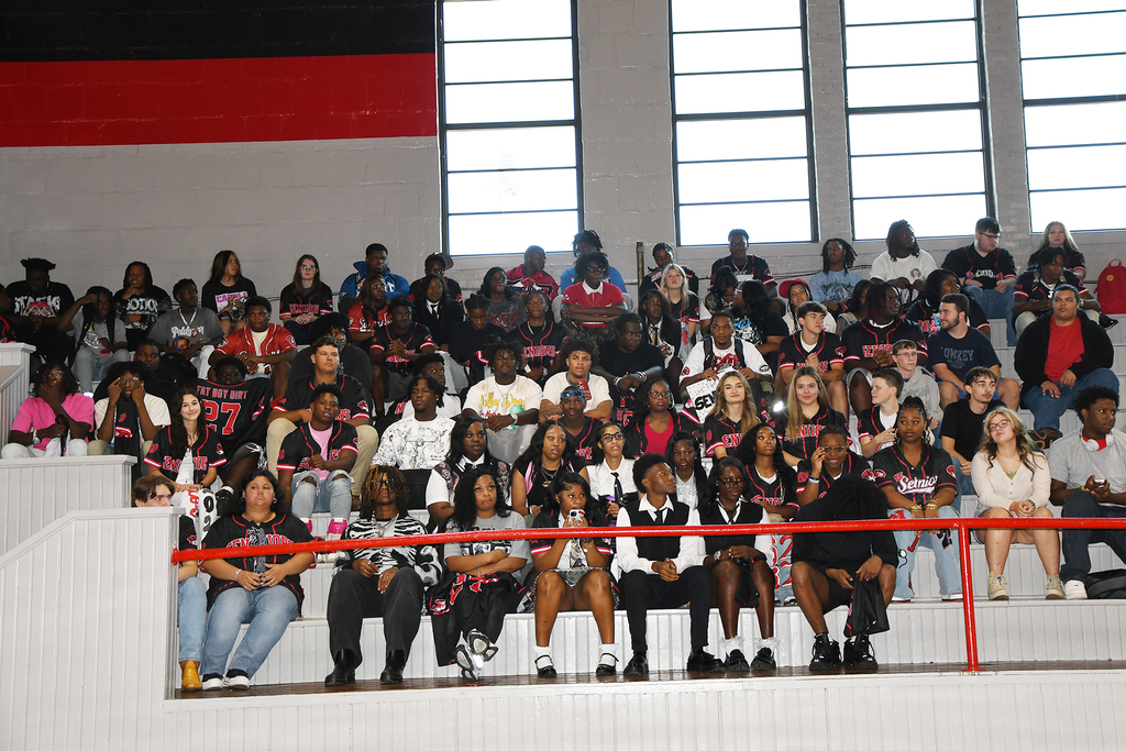 A crowd of people in red and white attire sitting in stadium bleachers, some wearing hats and sneakers.