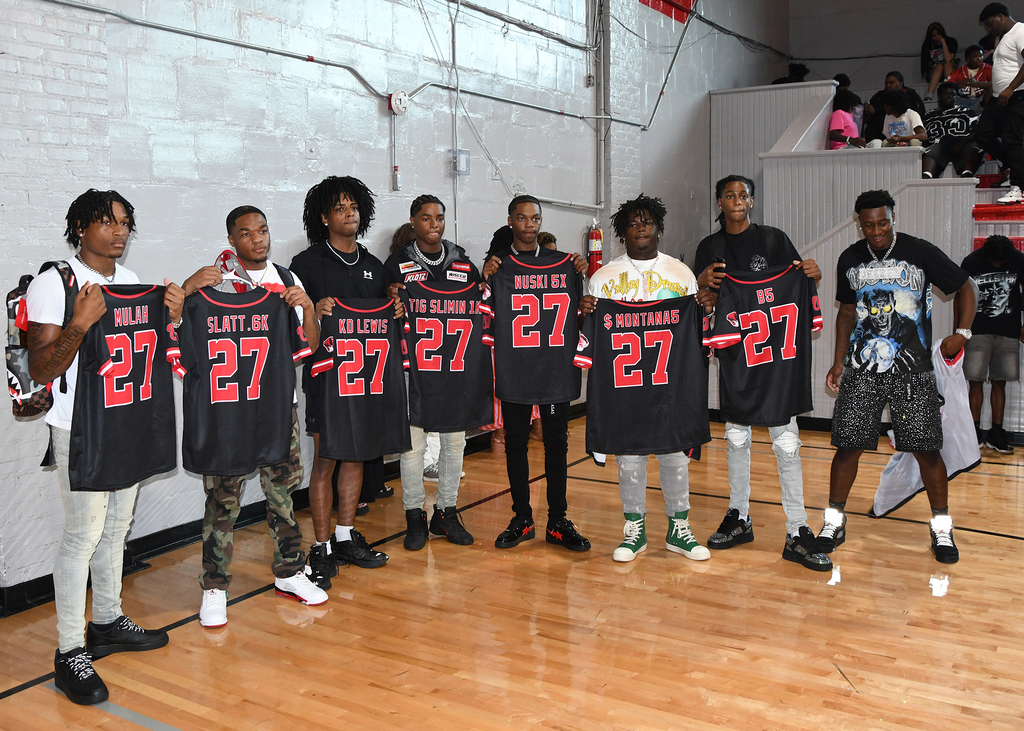 Group of people in black jerseys with number 27 hold them up. They are on a basketball court.