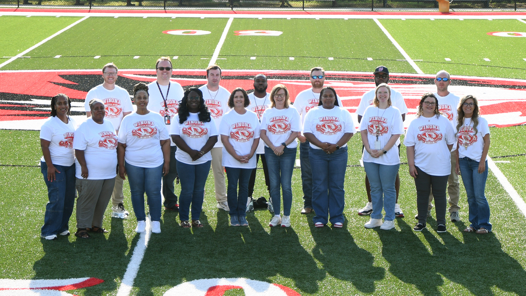 A group of people in white shirts pose for a photo on a football field with white lines.