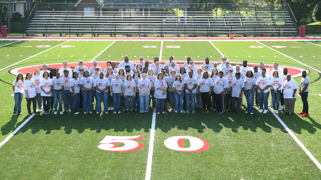 A group of people in white T-shirts and jeans standing on a football field. The number 50 is on the field.