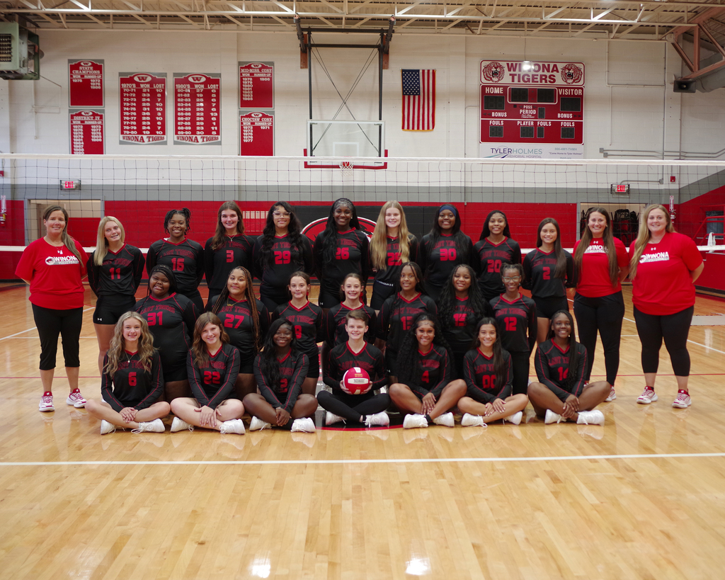 A group of people in black and red jerseys are posing for a photo on a basketball court.
