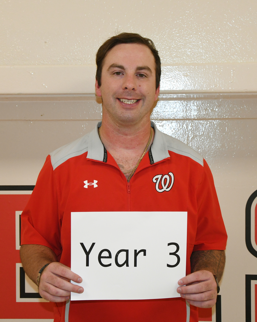 A person in a red shirt holds a sign with "Year 3" on it. The background is white with red and black logos.