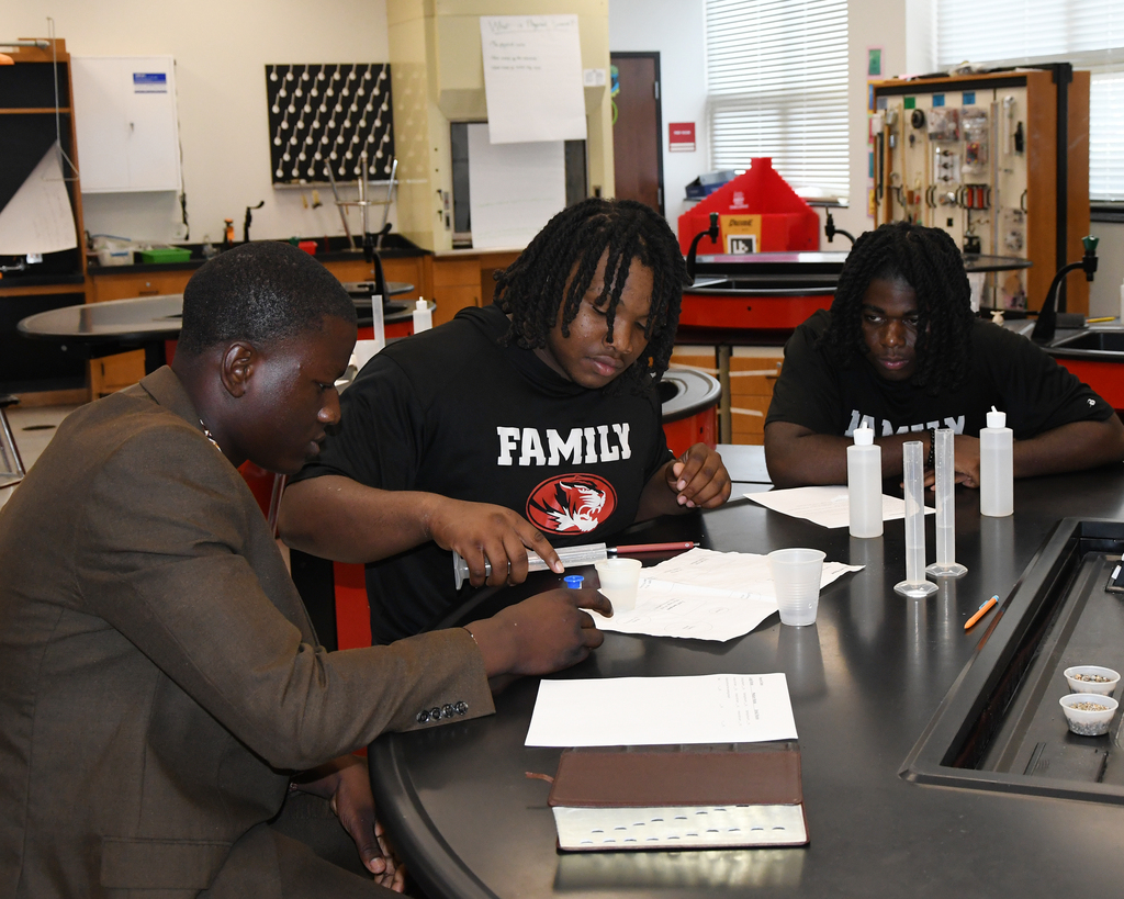 Three men in a lab setting, working with papers and scientific equipment on a table.