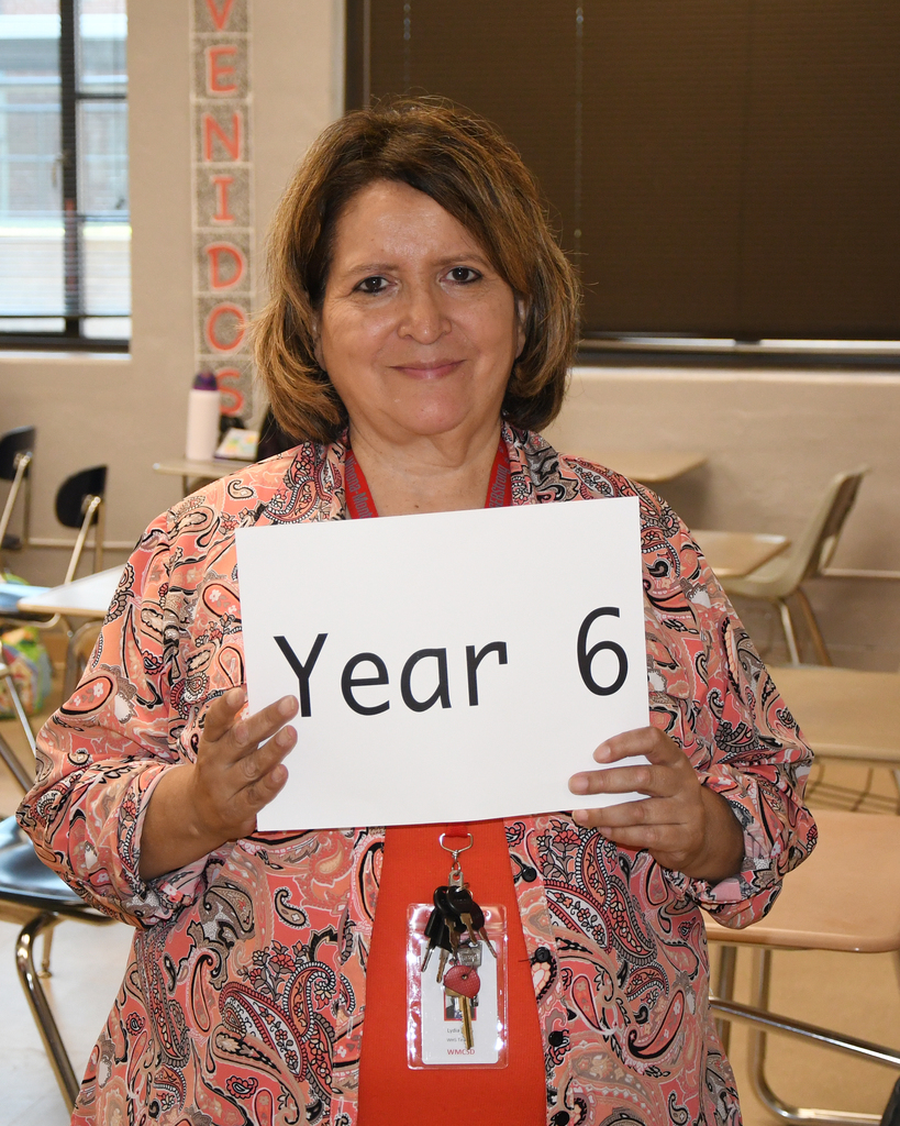 Woman with short brown hair holding a white sign with black text reading "Year 6".