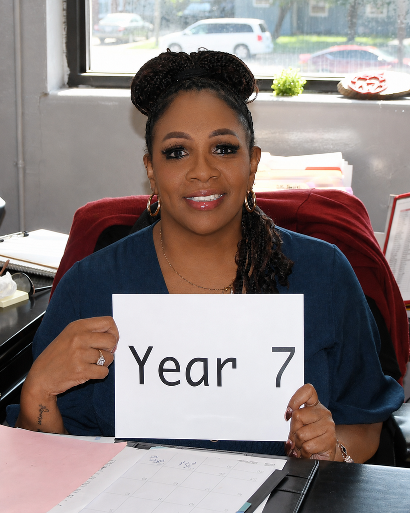 Woman in a blue shirt holding a white sign with "Year 7" written on it.