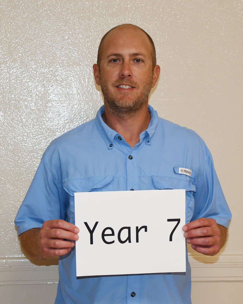 A man holds a white sign that reads "Year 7" against a plain white background.