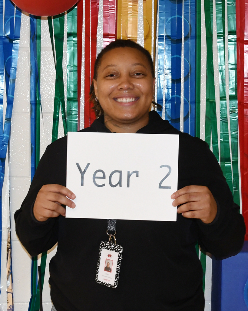 Person holding a white sign with "Year 2" in front of a colorful banner with Legos.