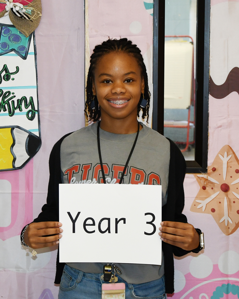 A young person wearing a gray shirt holds a white sign that says "Year 3" against a colorful background.