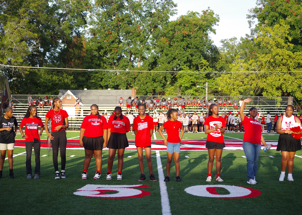 Group of individuals in red shirts and shorts on a football field. Two numbers, 5 and 0, are painted on the field.