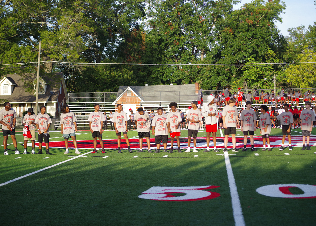 A group of players stands on a football field with white lines. Numbers "50" and "0" are on the field.