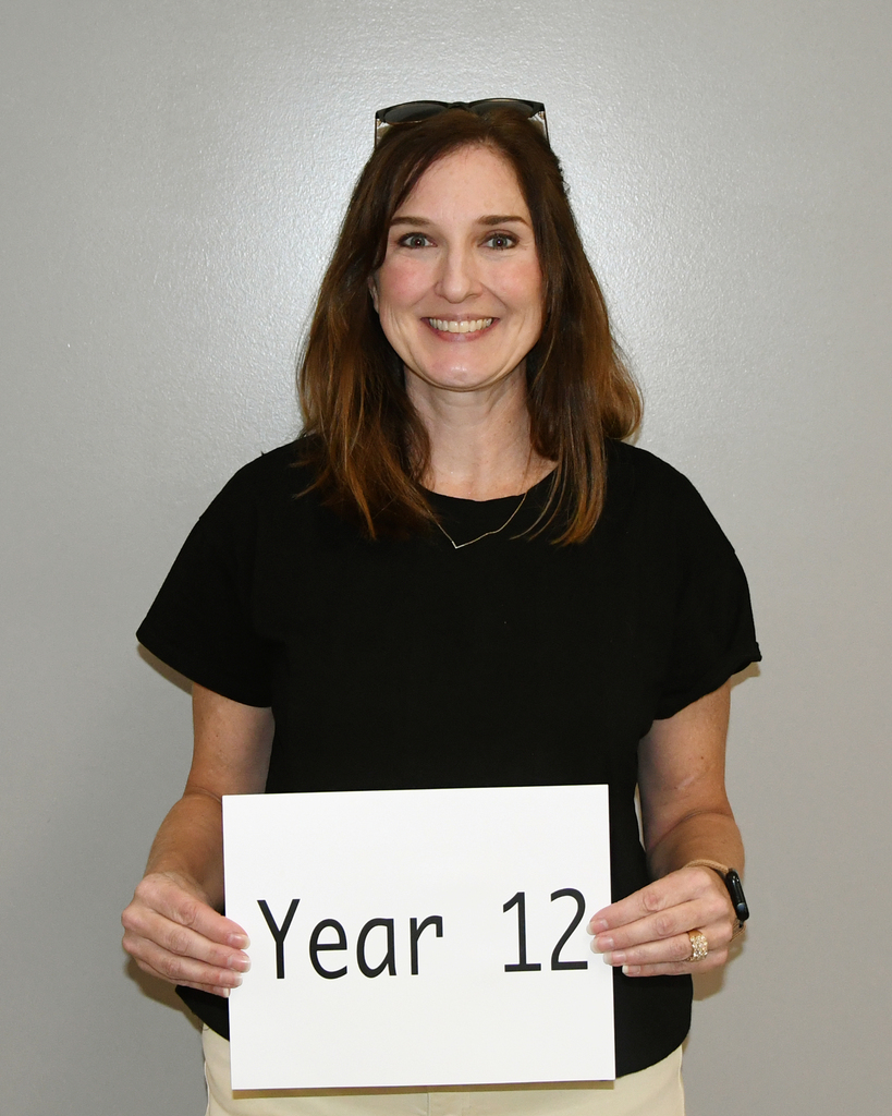 A woman in a black top holds a white sign with black text, "Year 12" against a light gray background.