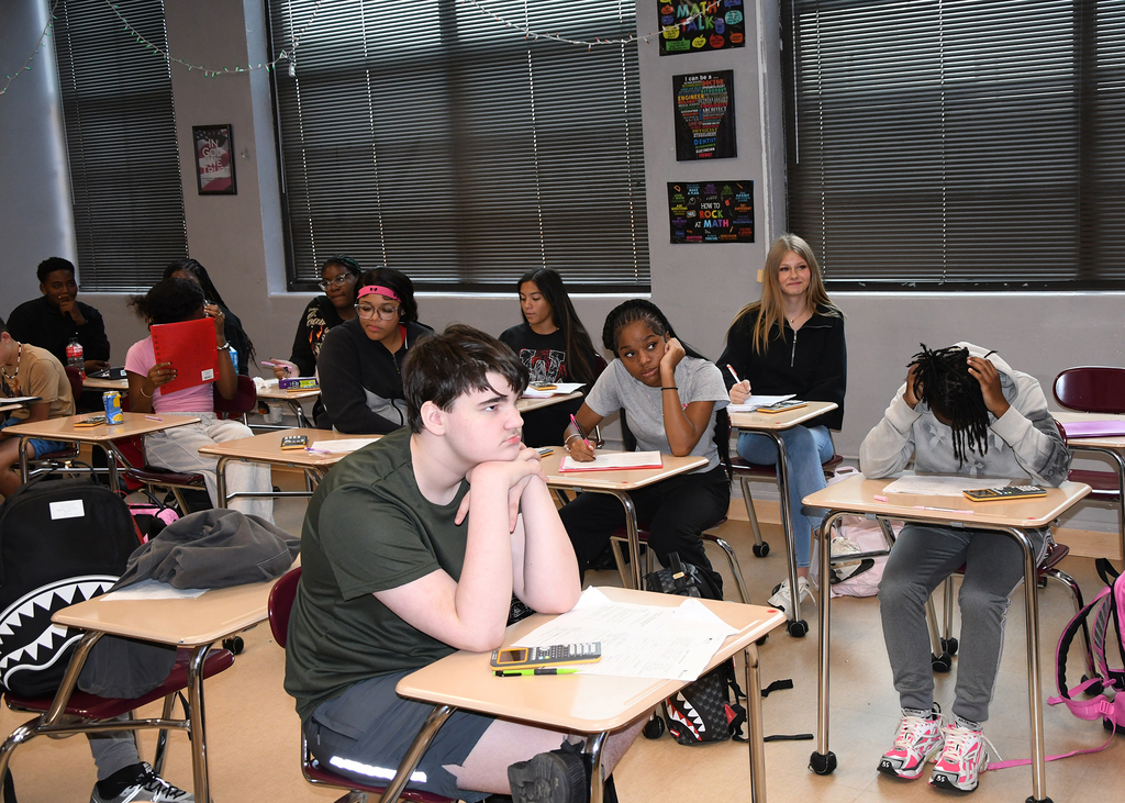 A classroom with desks; several students sitting, facing forward, with one person leaning back in their chair.