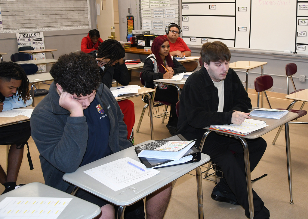 Students in a classroom, seated at desks, appear to be engaged in an examination or test.