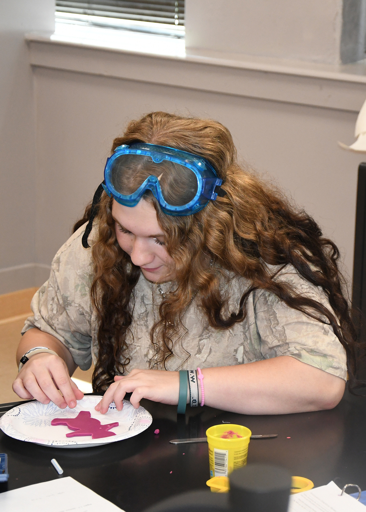 Person seated at a table wearing blue goggles, holding a paper plate with a pink star-shaped cutout.