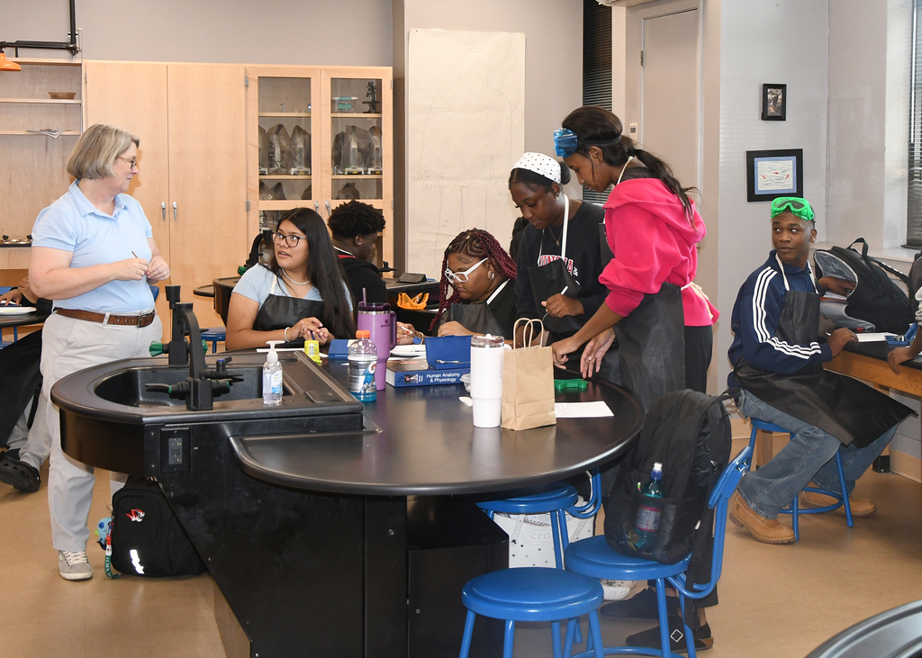 A group of students, some in aprons, work together around a table in a classroom setting.