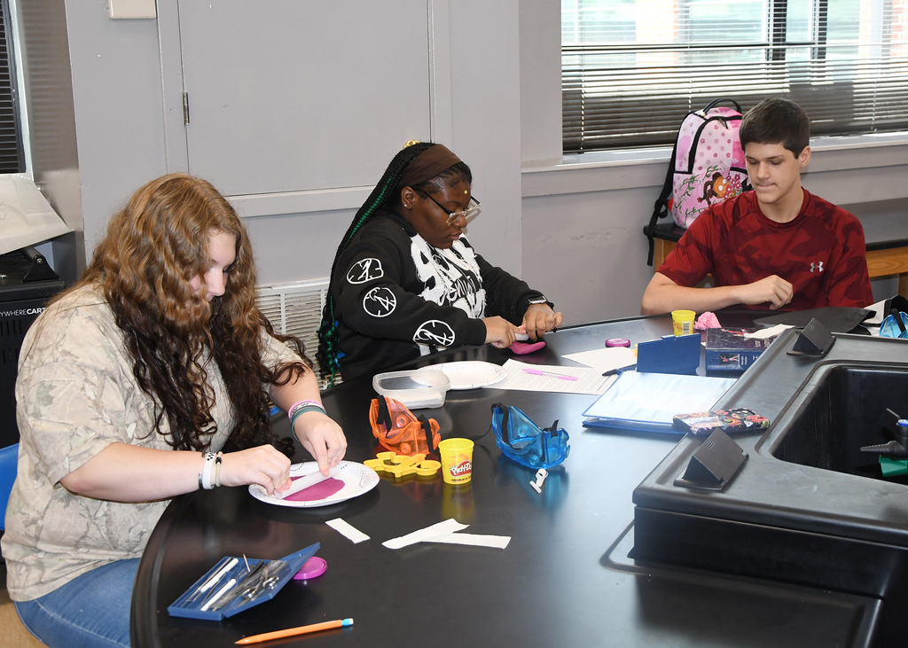 Three individuals work together at a table, crafting with paper, scissors, and other art supplies.