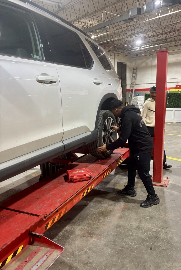 A man is working on a white SUV in a garage, lifting a tire with a jack.