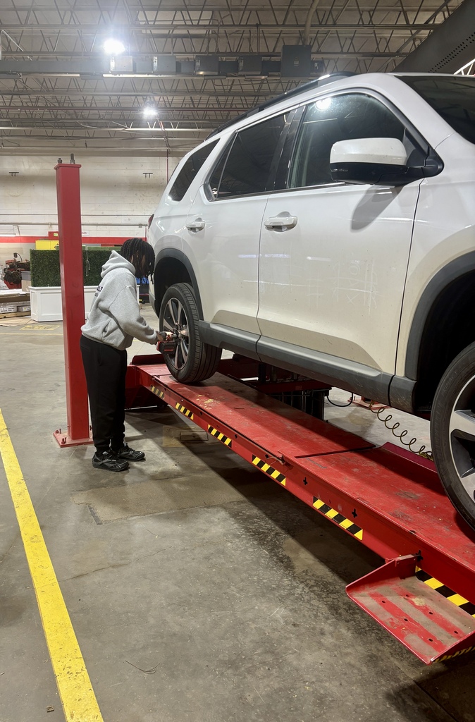 A person works on a white SUV in a garage, lifting the vehicle on a red platform.