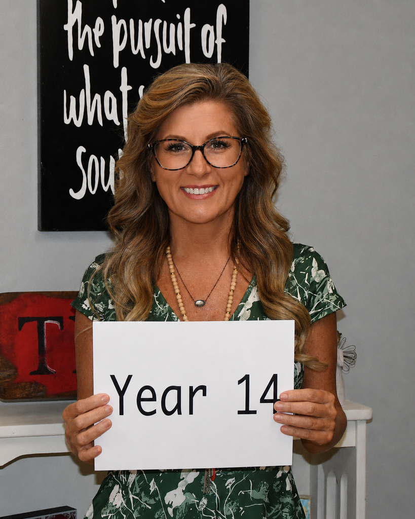 Woman holding a sign that says "Year 14" in front of a white wall with a black banner.