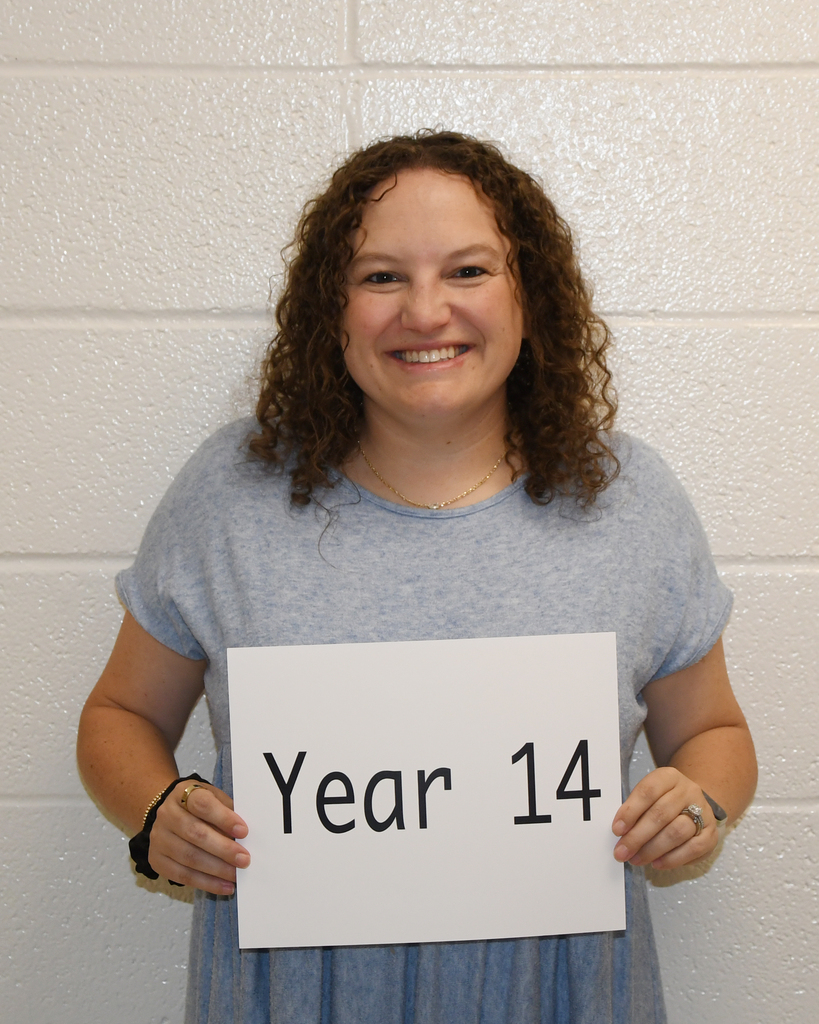 Woman in a blue shirt holding a white sign that reads "Year 14" against a white background.
