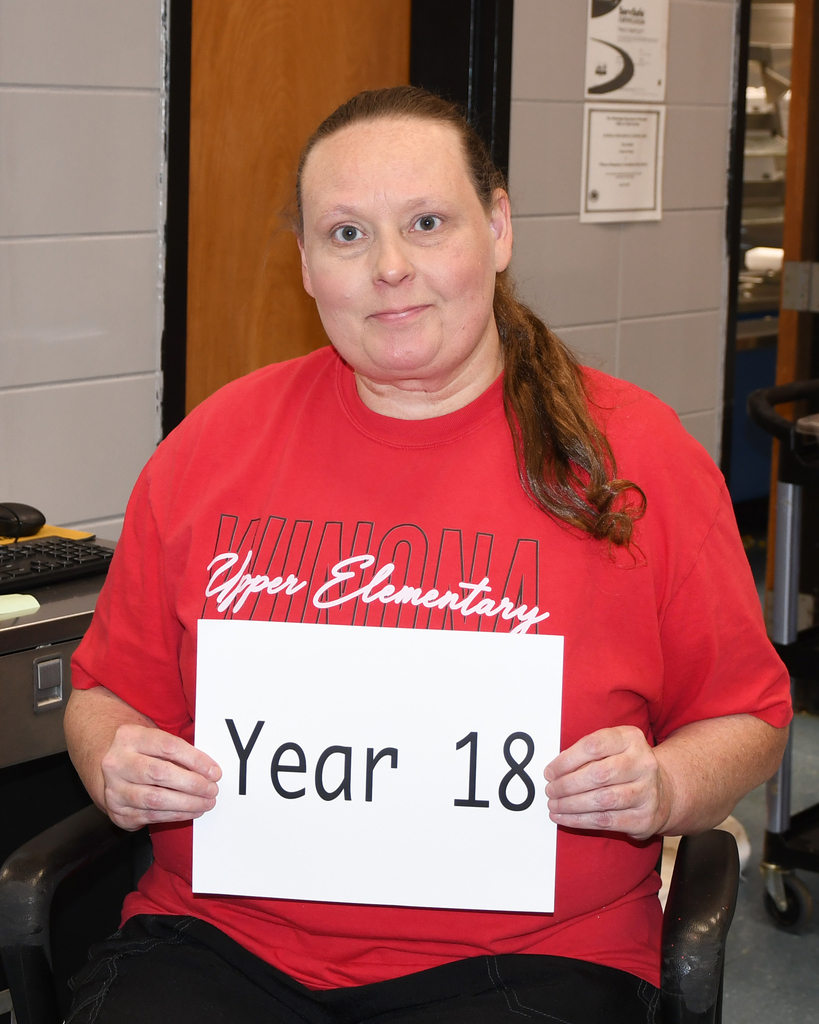 A woman in a red shirt with "Kings Mountain Upper Elementary" holds a sign that says "Year 18".