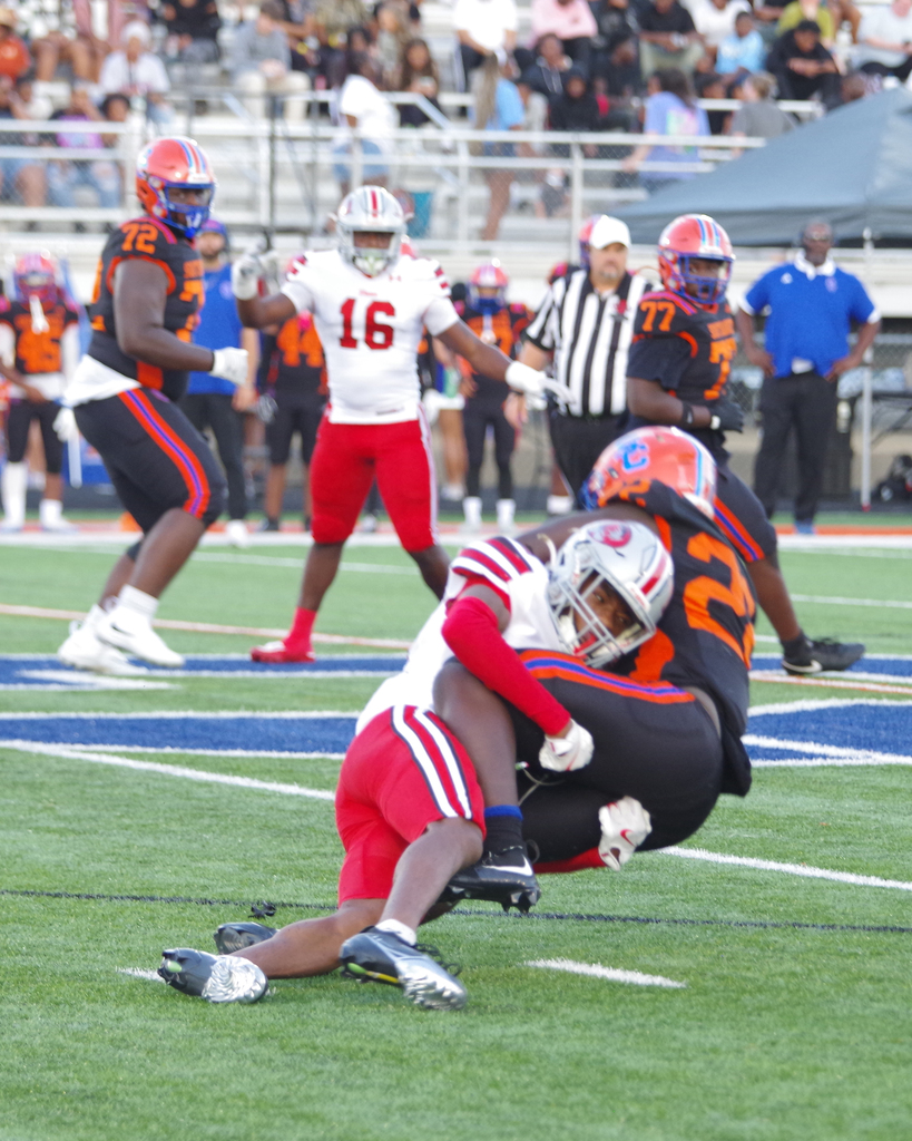Football players on a field, two in mid-tackled action. One player wears a white jersey with the number 16, another in red.