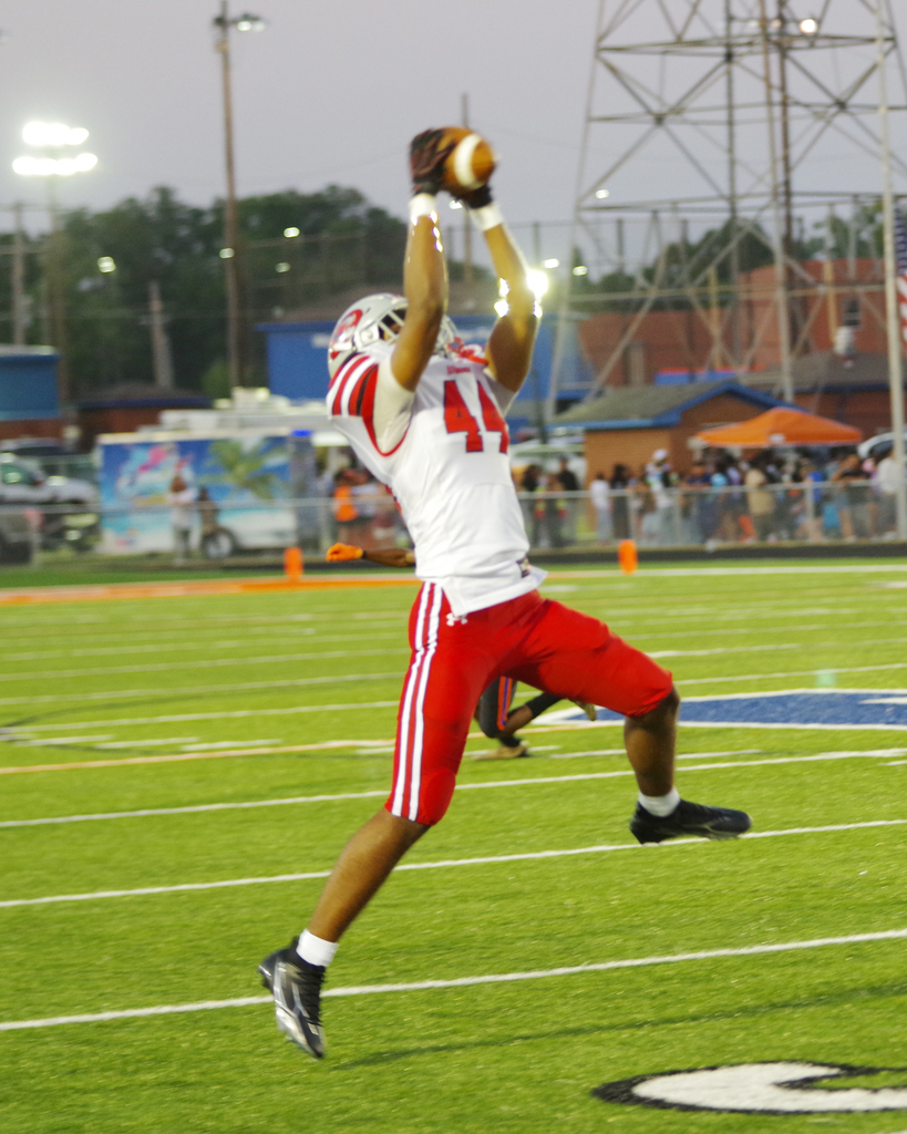 A football player in a white jersey and red shorts catches a ball mid-air on a football field.