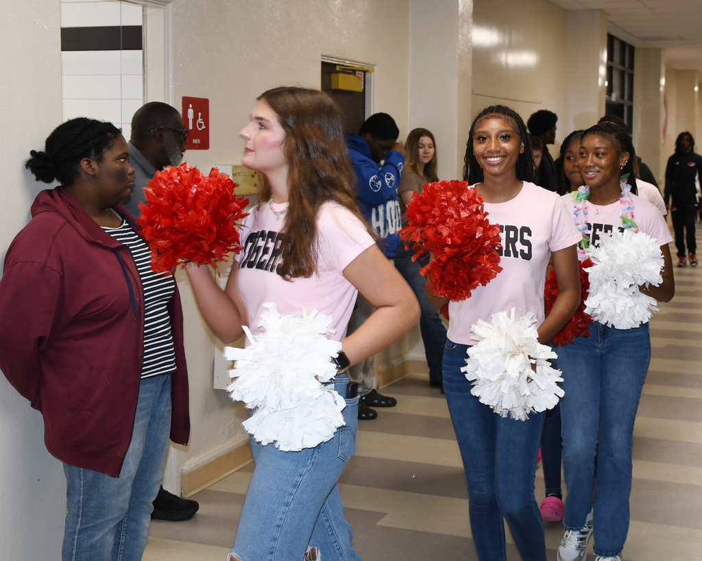 Four young women, two holding red and white pom-poms, in a hallway. Two women look ahead, two look back.
