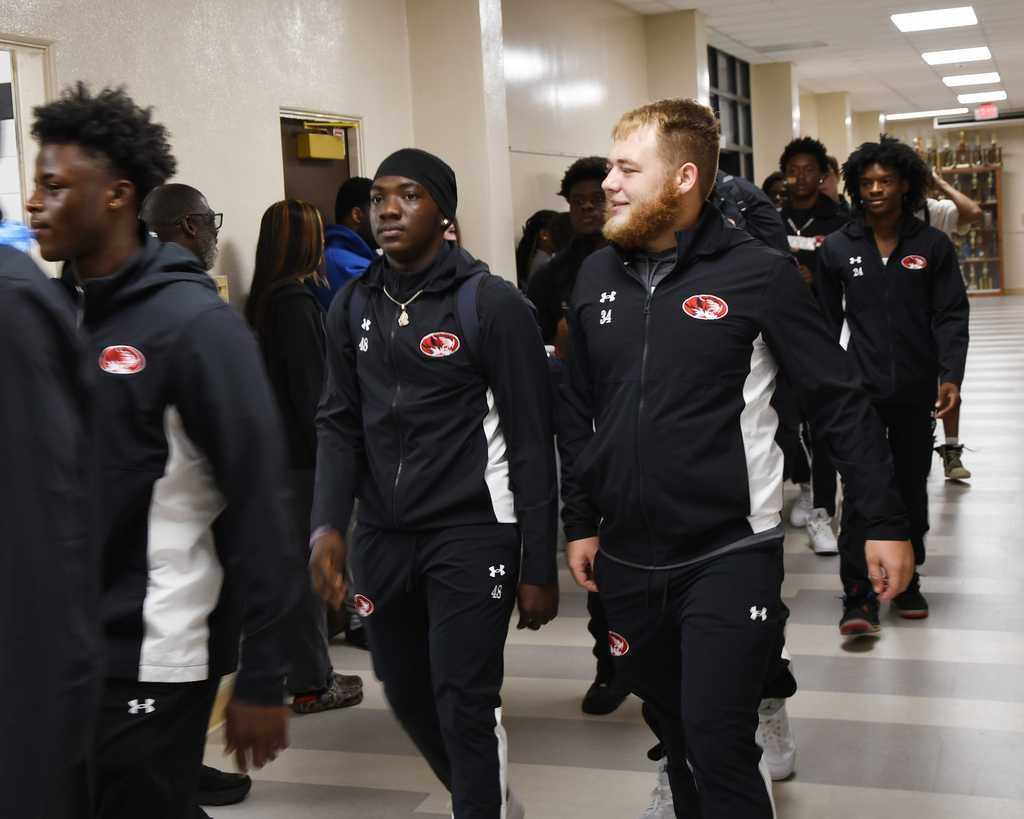A group of athletes in matching black and white uniforms walk down a school hallway.