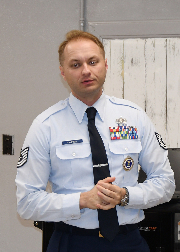 A man in a military uniform with several medals on his chest stands with hands clasped in front.