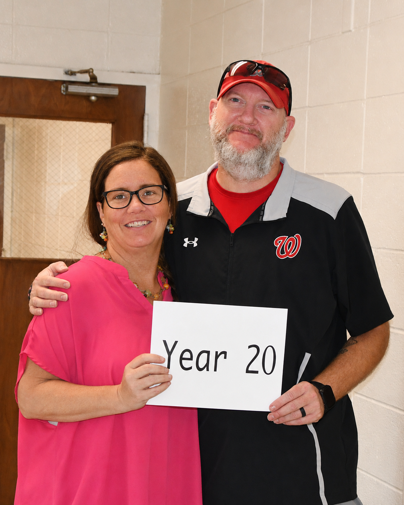 A man and a woman hold a white sign reading "Year 20" with a white background. They are standing close together.
