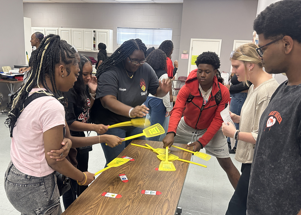 A group of young people playing a game with yellow paddles on a wooden table in a room.