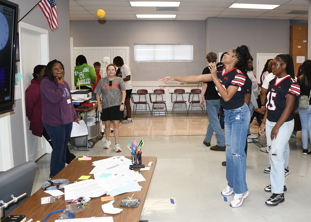 Indoor room with tables, papers, and people. Two women in front appear to be engaged in a game.