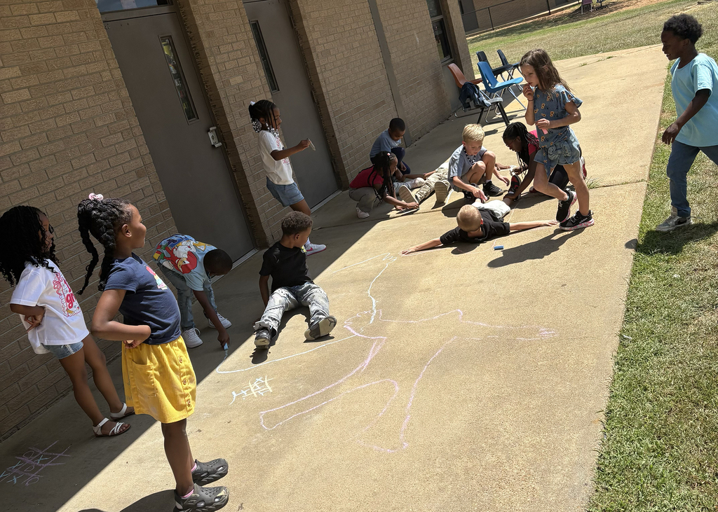 Children play and interact on a sidewalk, some standing and others sitting or lying on the concrete.