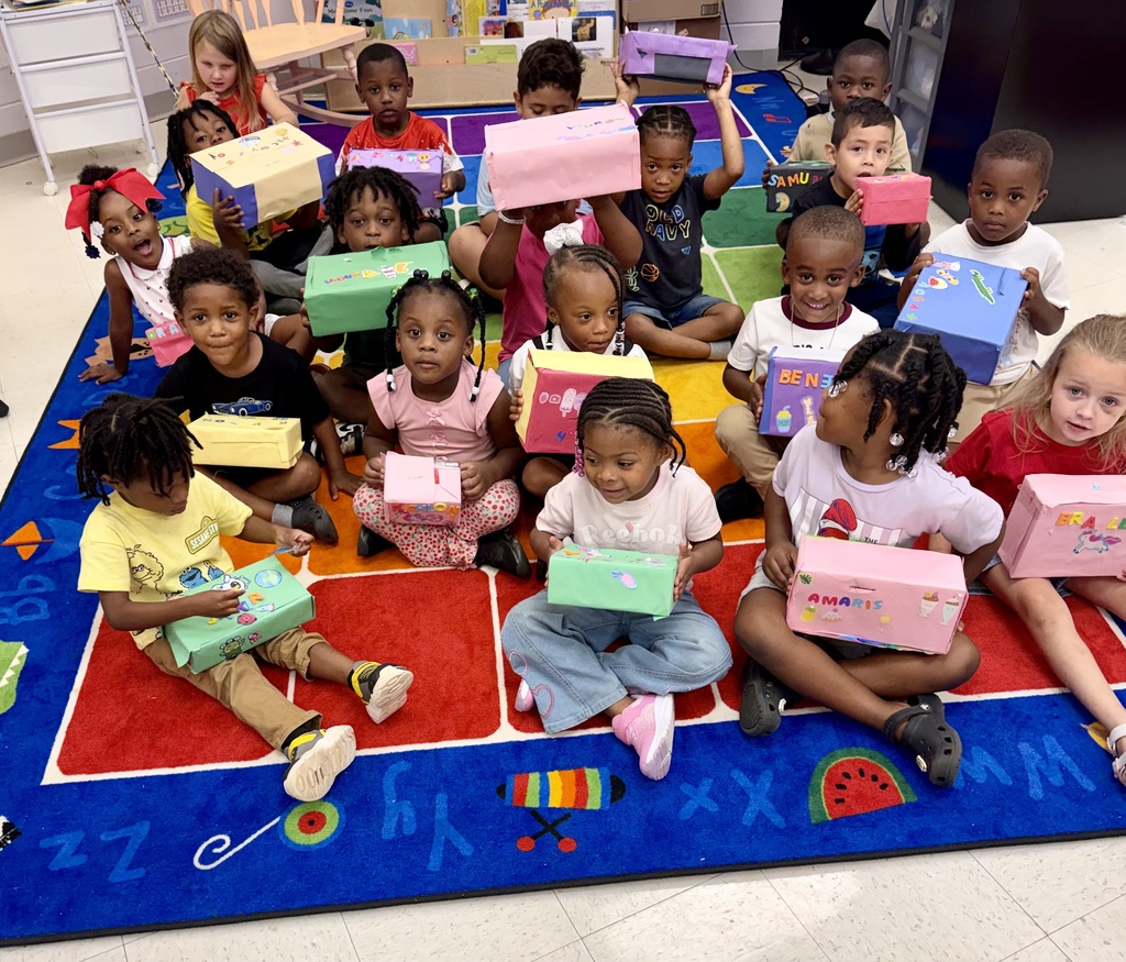 Children sitting in a circle on a carpet holding up boxes of gifts.