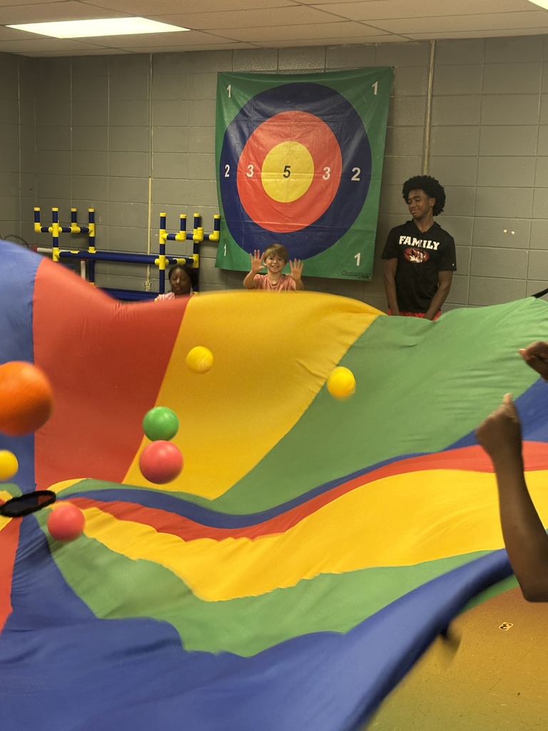 People play with multicolored balls in a gymnasium. An adult stands behind an inflated wall.
