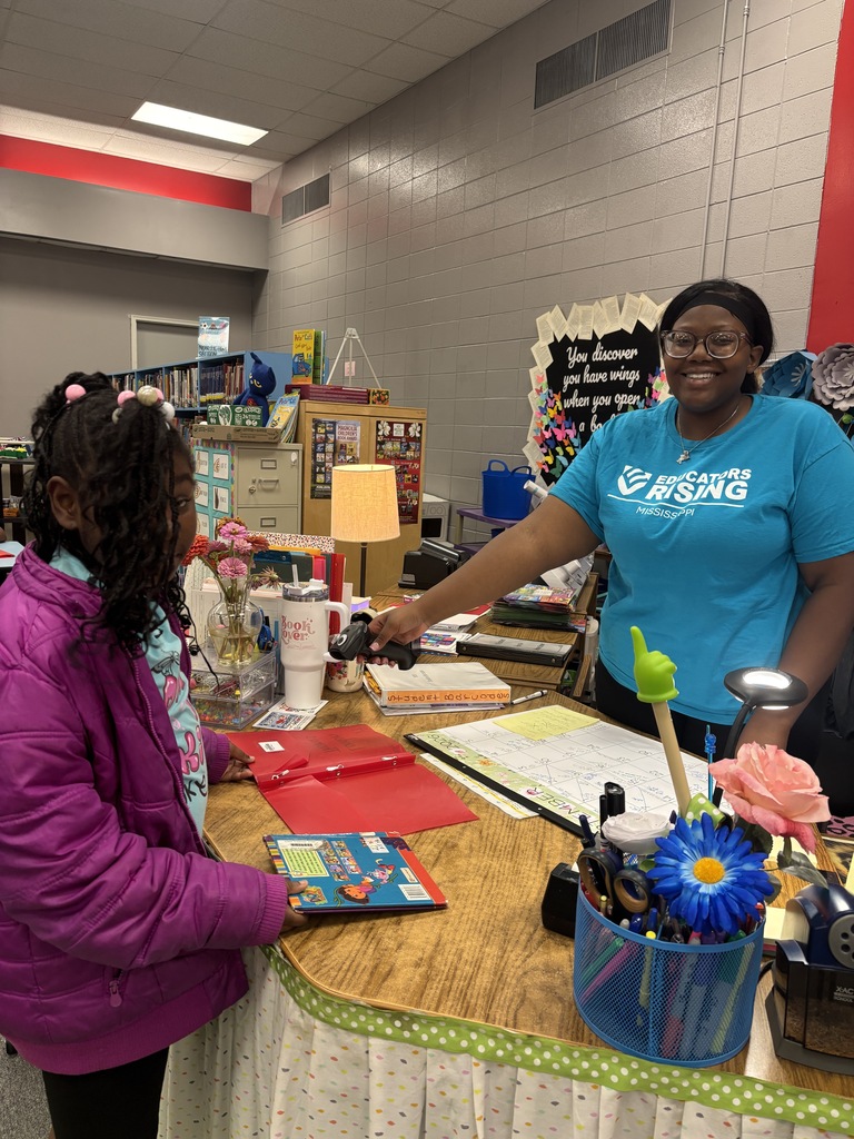 A woman in a blue shirt stands behind a counter, helping a girl in a pink jacket.