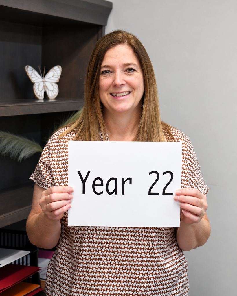 A woman holding a sign that reads "Year 22" with a shelf in the background.
