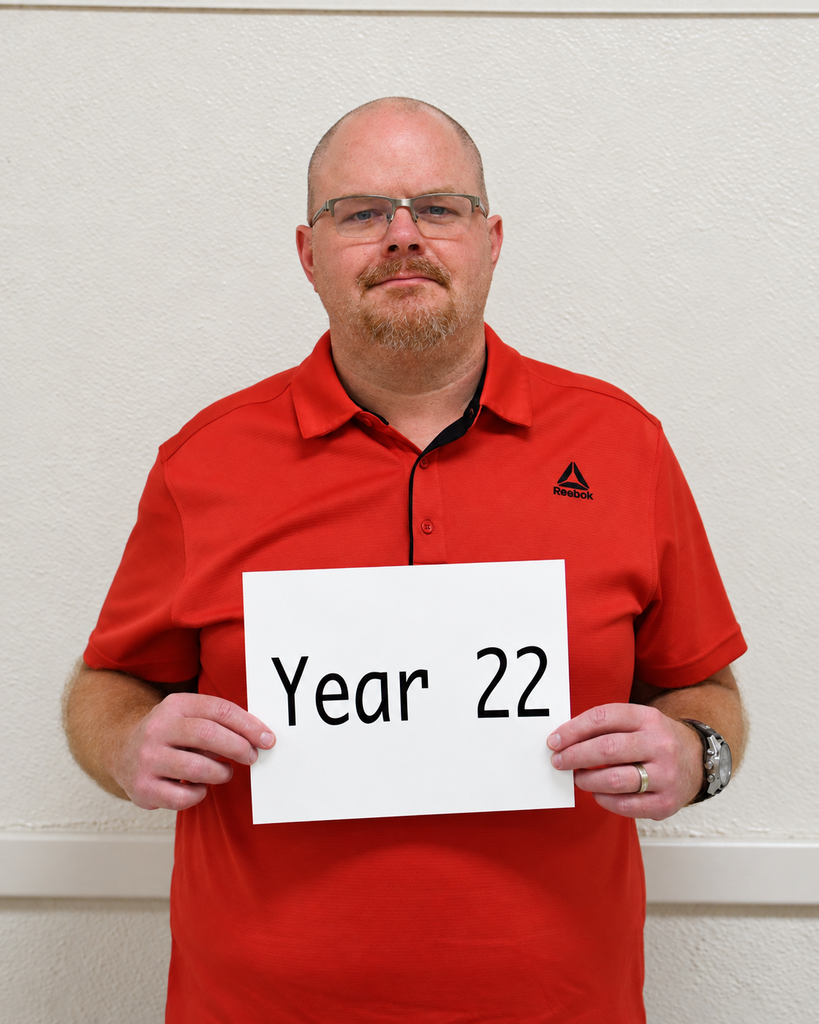 Man in a red shirt holding a sign that reads "Year 22." He wears glasses and a watch.