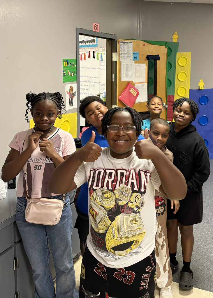 Children in a classroom, one smiling and making a peace sign, surrounded by peers, with colorful decorations in the background.