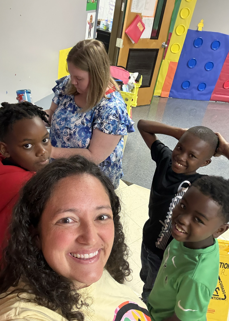 A group of children and two women in a playroom. One child smiles at the camera.