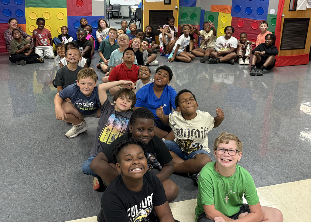 Group of children sitting on floor, posing for picture, colorful blocks in background.
