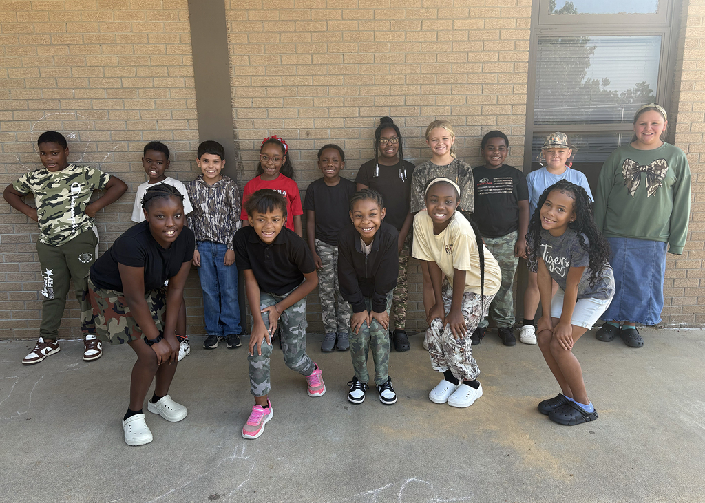 A group of children in varied attire standing in front of a brick wall with a window.
