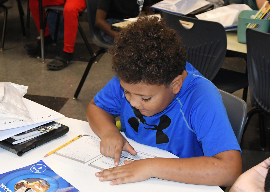 A child in a blue shirt sits at a table, working on a piece of paper.
