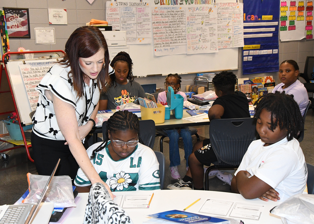 Teacher helping a student. The teacher wears a black and white blouse. Two students wear glasses.