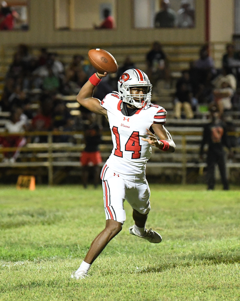 A football player in white and red uniform with number 14 runs and throws a pass on a grass field.