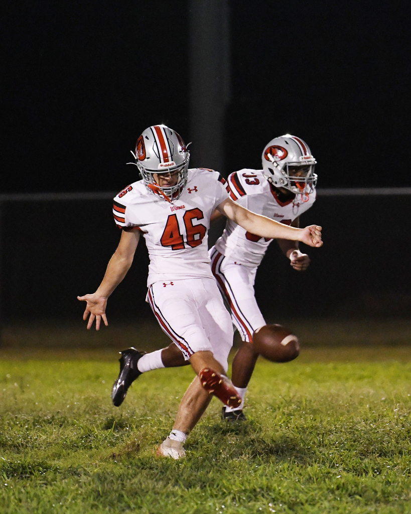 Two football players run on a grassy field. One wears white uniform with number 46 and the other in white with number 8.