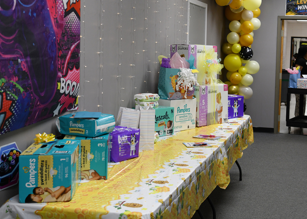 A room with a long table covered in a yellow tablecloth with white designs. Various gift boxes are displayed.